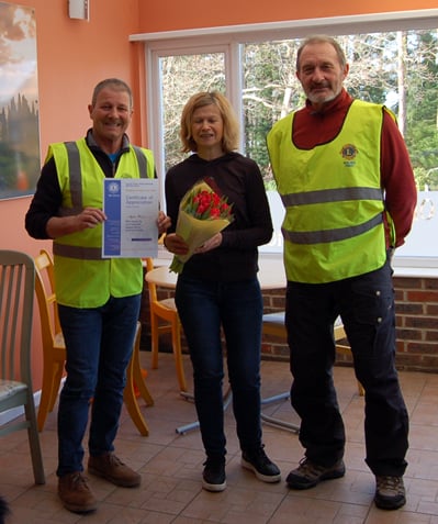 Jayne Brice, owner of The Old Dairy Coffee Shop in Bordon, receives a Certificate of Appreciation and a bouquet of flowers from Woolmer Forest Lions John Lewis and Vic Machin