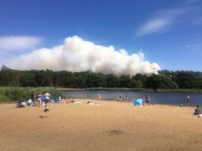 Onlookers watch a plume of smoke rising above Hankley Common from nearby Frensham Little Pond