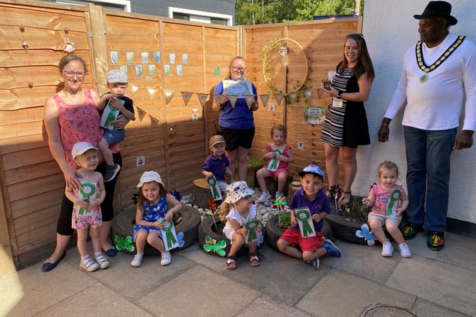 Whitehill town mayor Cllr Leeroy Scott, right, presents Town in Bloom rosettes and certificates to children at Tiny Tops nursery, Wolfe Lodge, Farnham Road, Bordon, August 10th 2022.