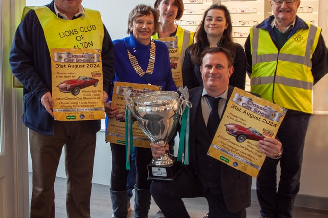 The 21st Alton Classic Car Show is launched with the trophy going on display at major sponsor Specsavers. From left: Alton Lions John Mill, Moira Baker (president), Lisa March and Mike Baker, with Specsavers optical assistant Chloe Knight and Dean-Paul Phillips (kneeling), chief executive of The Little Grey Cells, April 2024.